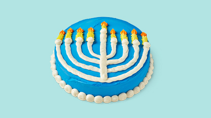 This is an image of a cake decorated to look like the hanukkah menorah, which features nine candle holders lit by candles. The cake has blue frosting and a round shape, sitting against a plain background.