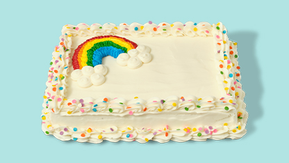 A rectangular cake decorated with colorful sprinkles and a rainbow shape on top. It's placed on a blue table cloth.