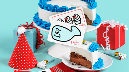 A colorful birthday cake with a whale decoration on top, surrounded by gift boxes and party accessories.